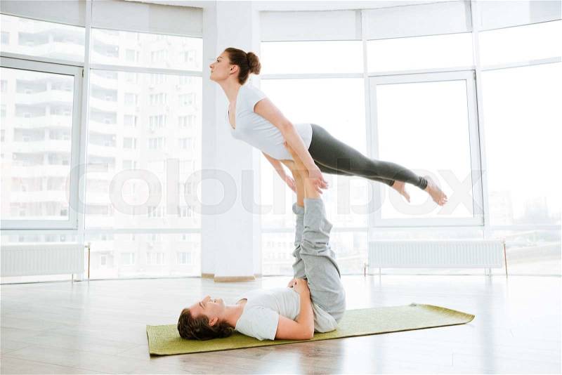 Beautiful young couple doing acro yoga in studio together, stock photo