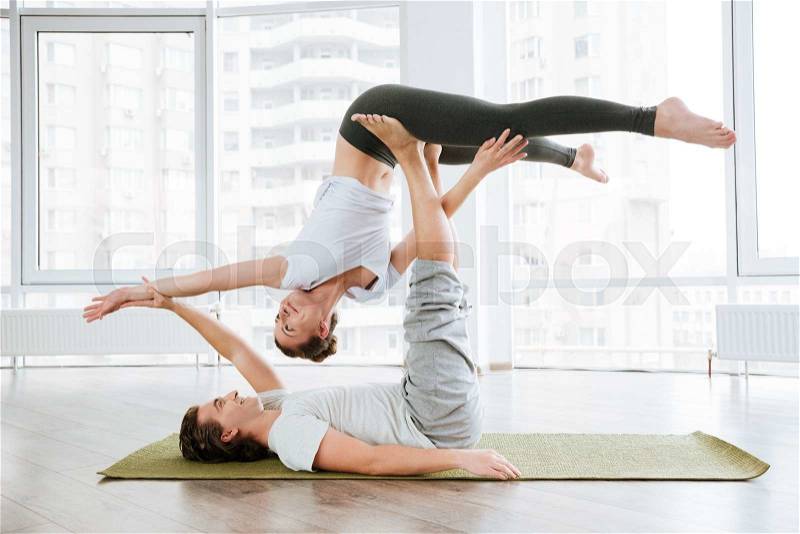Happy couple doing acrobatic yoga position in studio together, stock photo