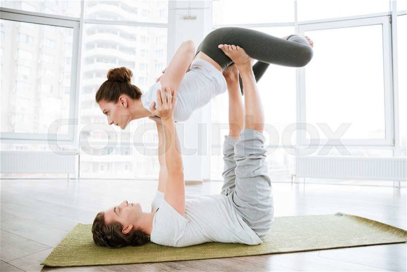 Man and woman doing acro yoga for couples in studio, stock photo