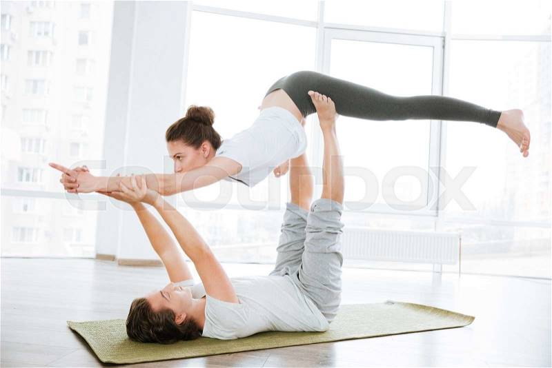 Young couple practicing acro yoga on green mat in studio together, stock photo