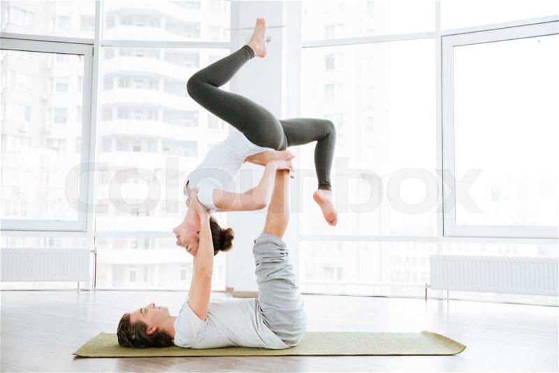 Pacified couple doing acro yoga in studio together, stock photo