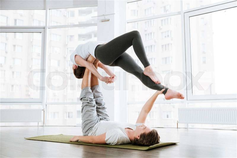Beautiful couple practicing acro yoga on green mat in studio together, stock photo