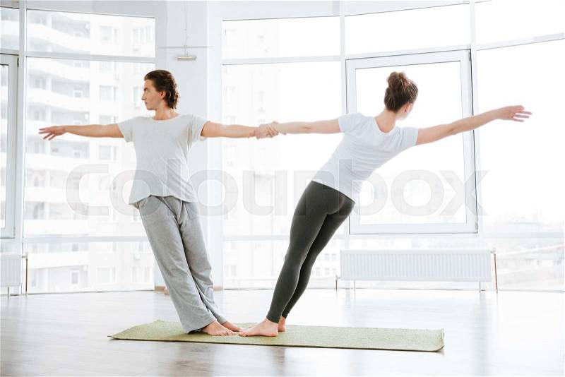 Young couple doing stretching exercises in yoga studio together, stock photo
