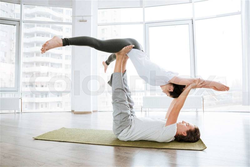 Peaceful young couple practicing acro yoga in studio together, stock photo
