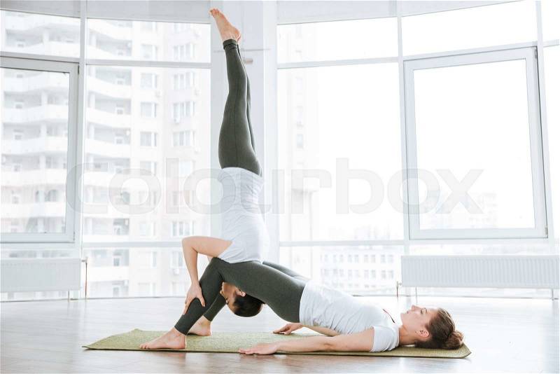 Two slim young women doing balancing pose on pink yoga mat, stock photo