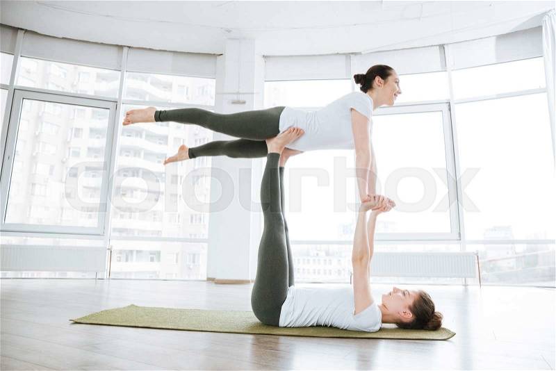 Two attractive young women balancing and doing acro yoga in studio, stock photo