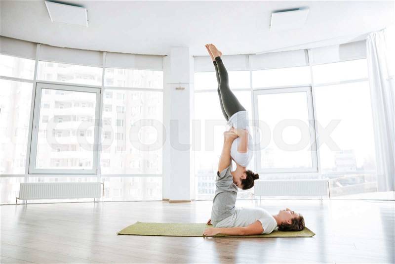 Beauiful couple practicing acro yoga on green mat in studio together, stock photo
