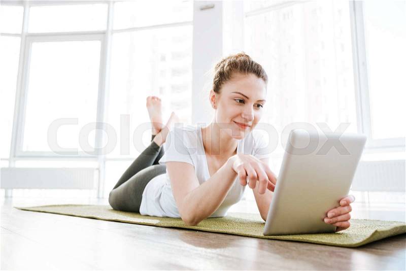 Smiling cute young woman using tablet in yoga studio, stock photo