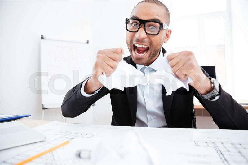 Angry businessman tearing up a document, contract or agreement in office, stock photo