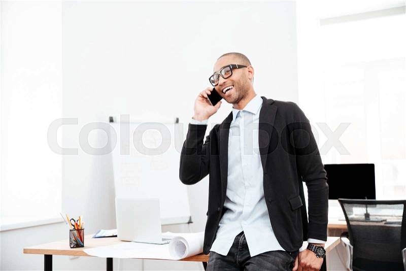 Young happy businessman talking on the cell phone in office, stock photo