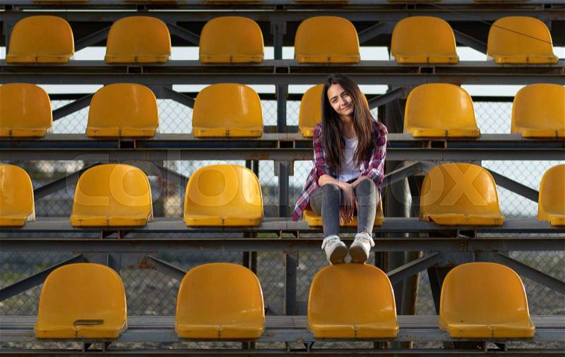 Lonely cheerleader girl sitting in the stands and smiles sweetly. front view, stock photo