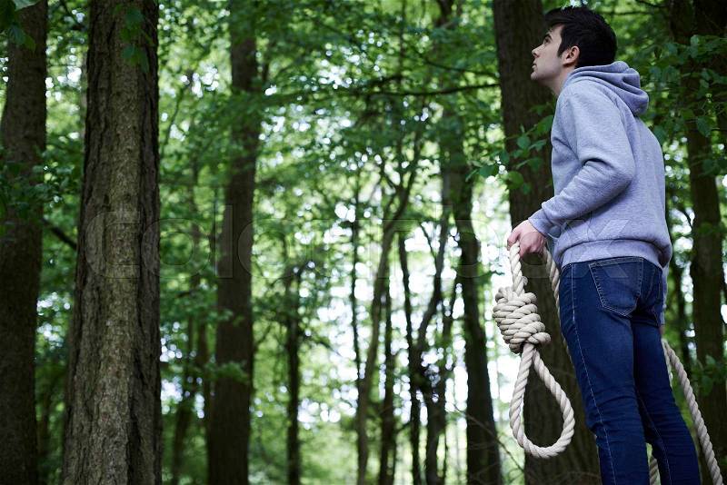 Depressed Man Contemplating Suicide By Hanging In Forest, stock photo