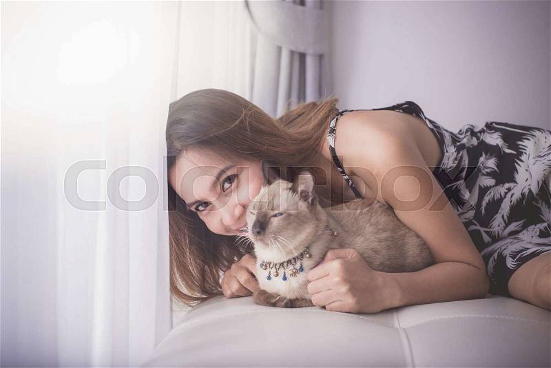 Asian woman and cat laying on sofa with window light, stock photo
