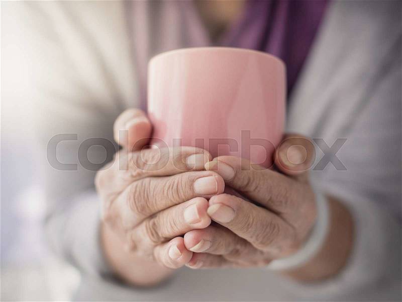 Old woman holding cup of hot coffee drink in her hands, stock photo