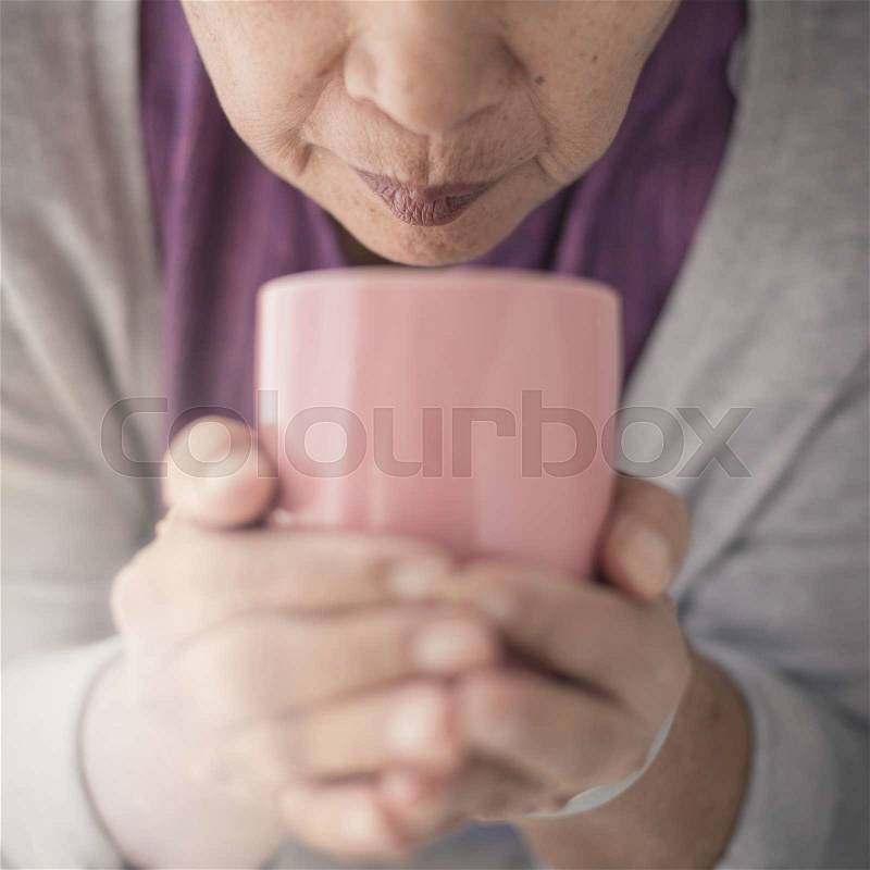 Old woman holding cup of hot coffee drink in her hands, stock photo