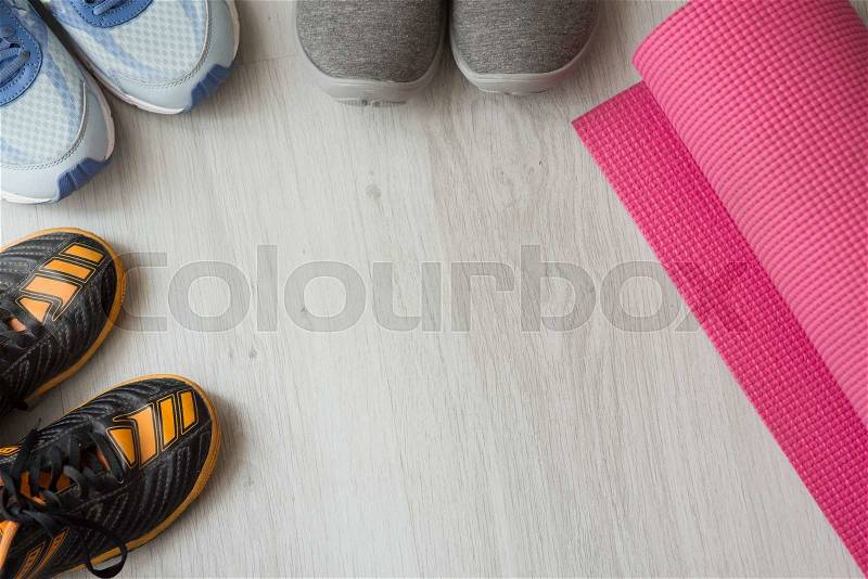 Orange, blue, and gray sport shoes with pink yoga mat on gray floor background, stock photo