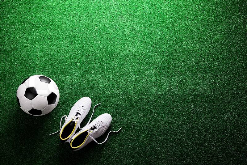 Soccer ball and cleats against artificial turf, studio shot on green background. Flat lay, copy space, stock photo