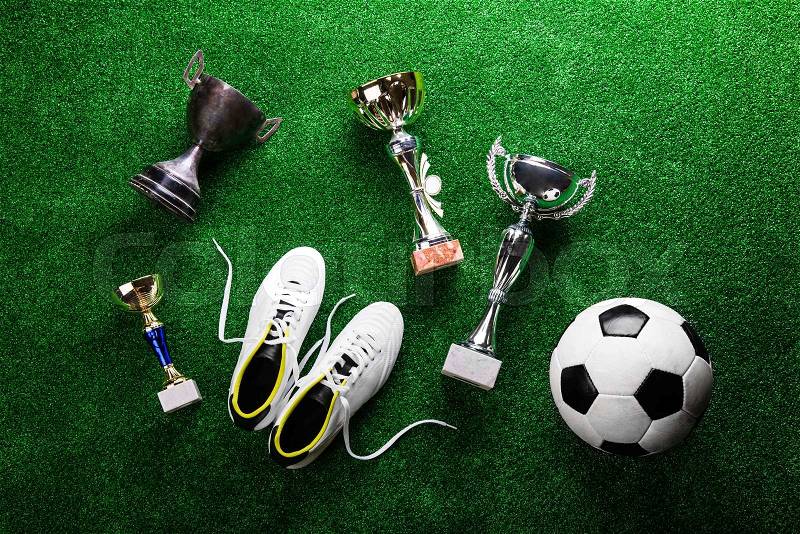 Soccer ball, cleats and various trophies and cups against artificial turf, studio shot on green background. Flat lay, stock photo