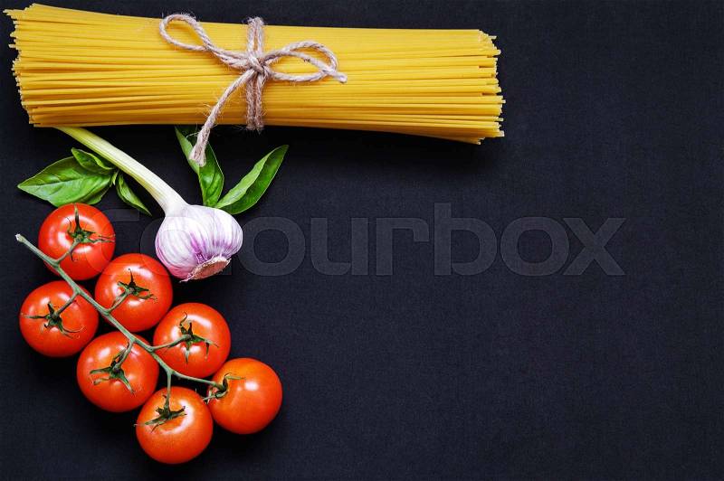 Food frame. Pasta ingredients. Cherry-tomatoes, spaghetti pasta, garlic, basil, parmesan and spices on dark grunge backdrop, copy space, top view, horizontal oriented, stock photo