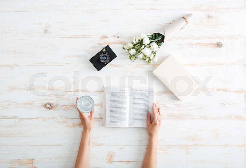 Women hands turn over book pages with glass of water, flowers and camera on the wooden desk, stock photo