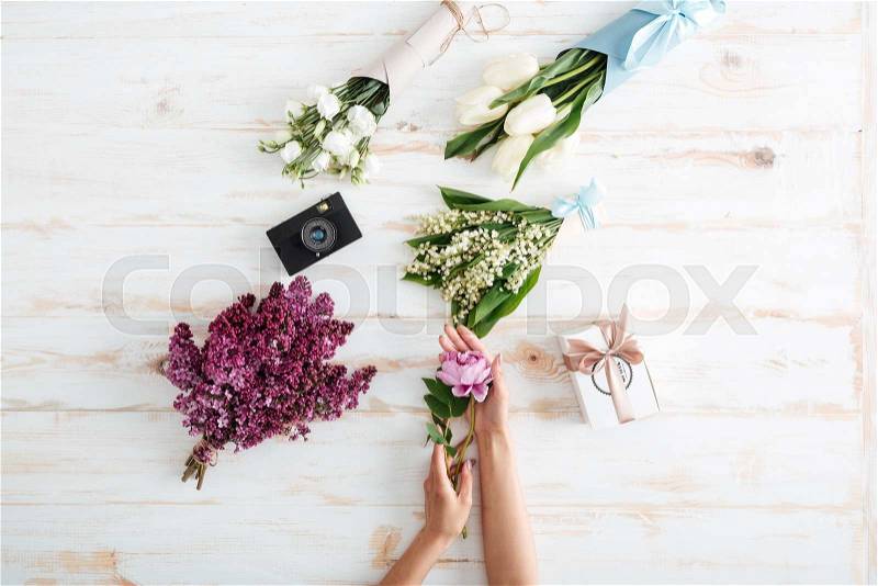 Hands of young woman choosing bouquet of flowers on wooden, stock photo