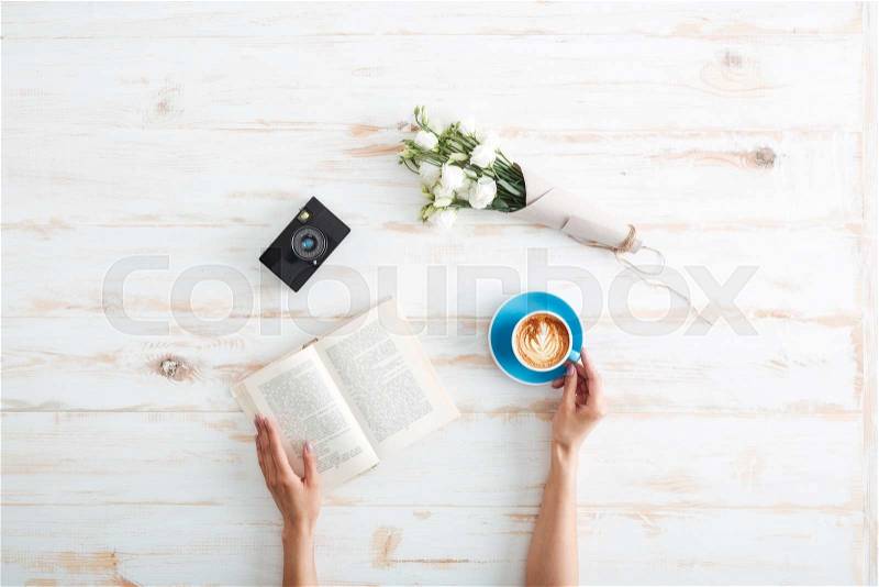 Female hands holding open book and coffee cup on the wooden desk, stock photo
