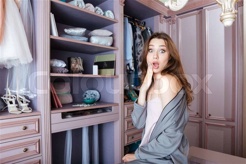 Beautiful young shocked woman don\'t know what to wear sitting in her closet, stock photo