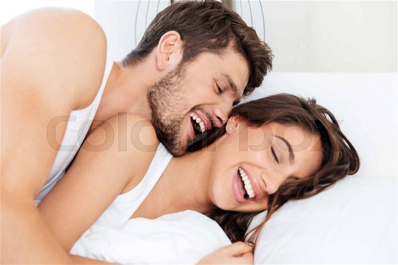 Happy beautiful young couple laughing together in the bed, stock photo