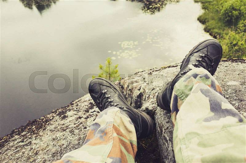 Male feet in camouflage pants and black rough shoes, travel background. Vintage tonal correction photo filter, old style effect, stock photo