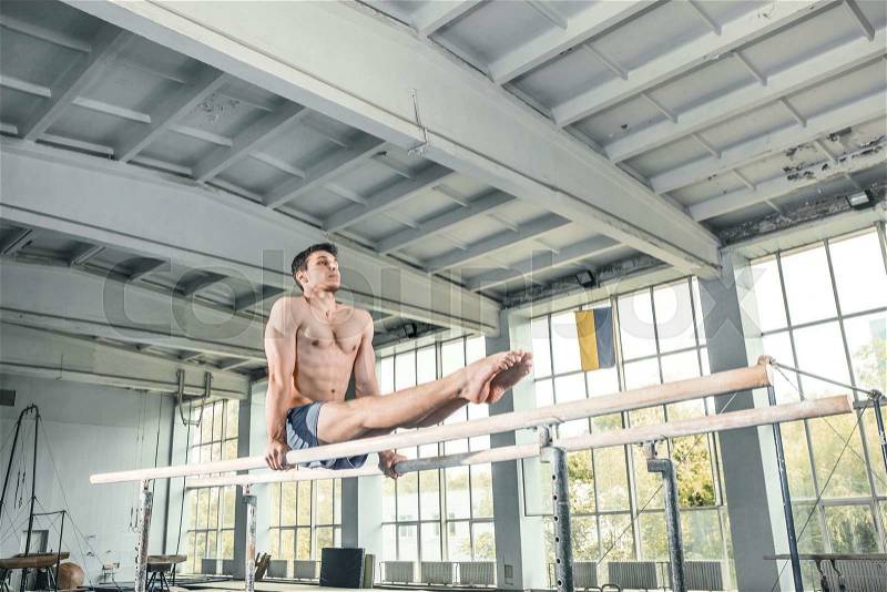 Male gymnast performing handstand on parallel bars at gym, stock photo