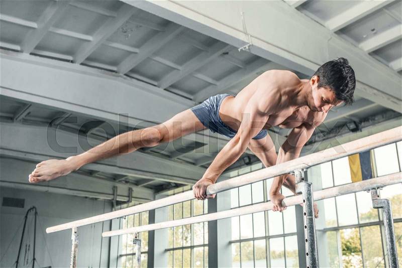 Male gymnast performing handstand on parallel bars at gym, stock photo