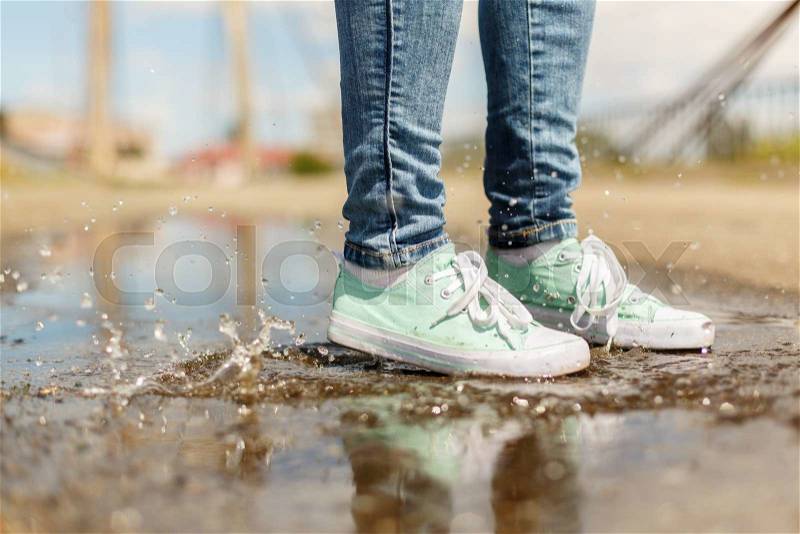 Woman in gumshoes jumping in a puddle. Close up shot of foots in a shoes with water splashes, stock photo