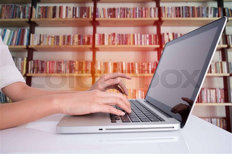Woman hand using laptop on white table with book shelf background, stock photo