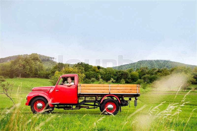 Young man driving red vintage pickup truck, green summer nature, stock photo