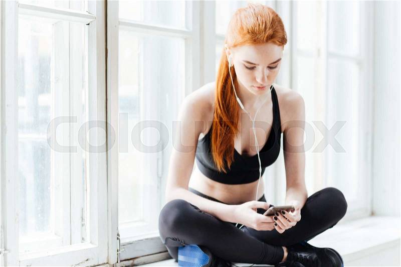 Close-up portrait of a pretty young fitness woman with smartphone at the gym, stock photo