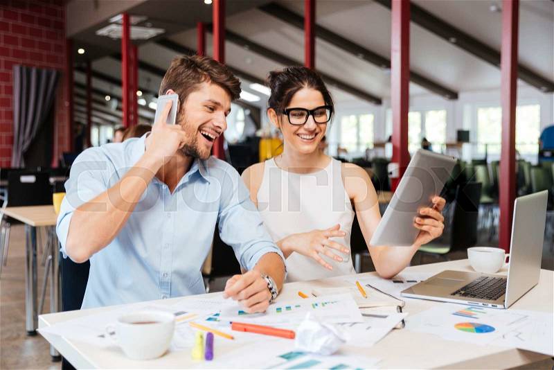 Happy beautiful young businesspeople talkign on cell phone and using tablet in office together, stock photo