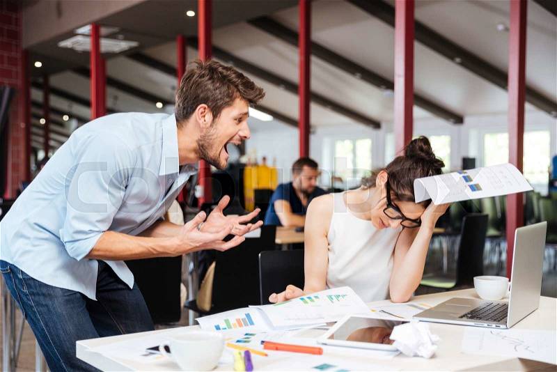 Mad crazy young businessman arguing with sad stressed businesswoman at work in office, stock photo