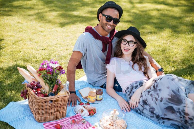Smiling young couple having picnic on the lawn in park, stock photo