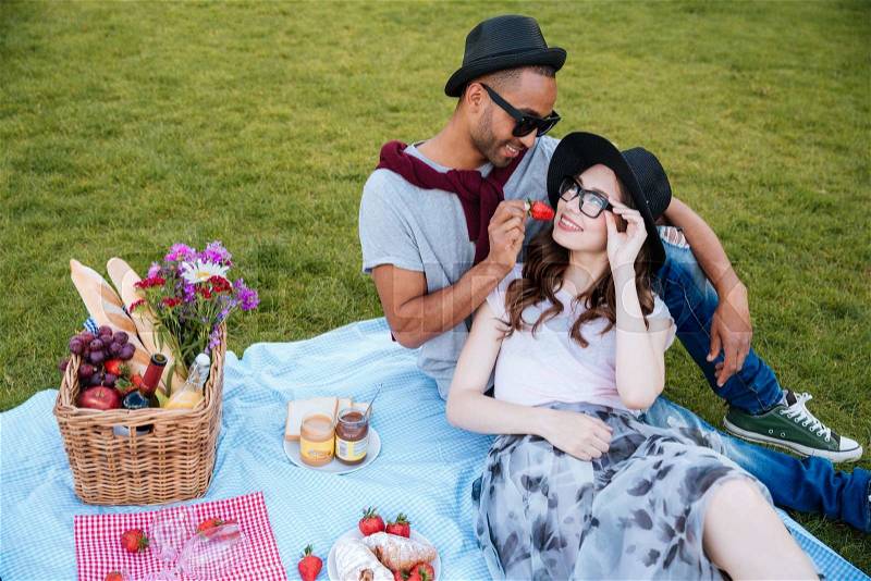 Tender young couple having picnic and eating fresh strawberry outdoors, stock photo