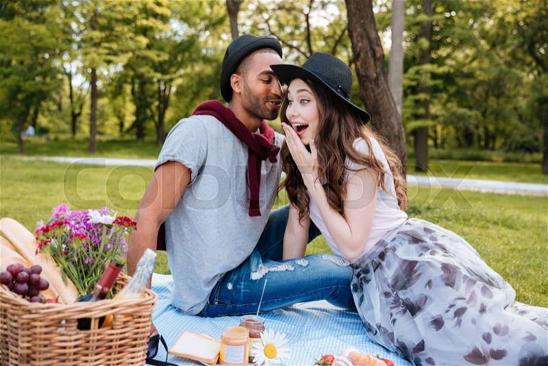 Amazed attractive young woman talking and having picnic with her boyfriend in park, stock photo