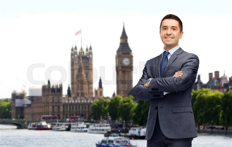 Business trip, people and office concept - happy smiling businessman in dark grey suit over london city background, stock photo