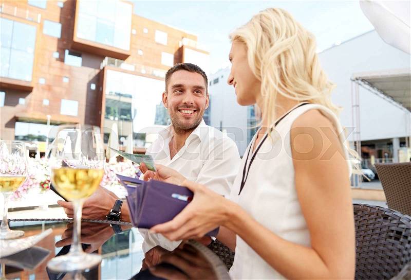 Date, people, payment and finances concept - happy couple with wallet and wine glasses paying bill at restaurant, stock photo