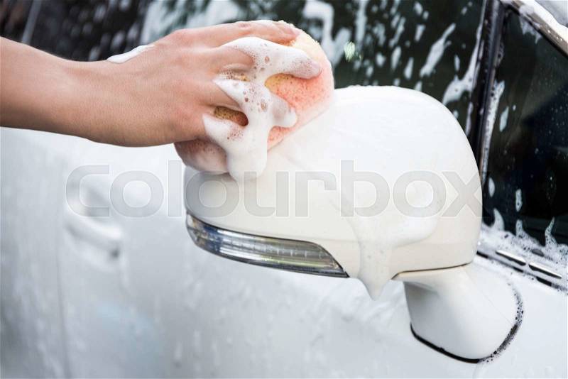 Car wash - male hand washing car mirror with sponge, stock photo
