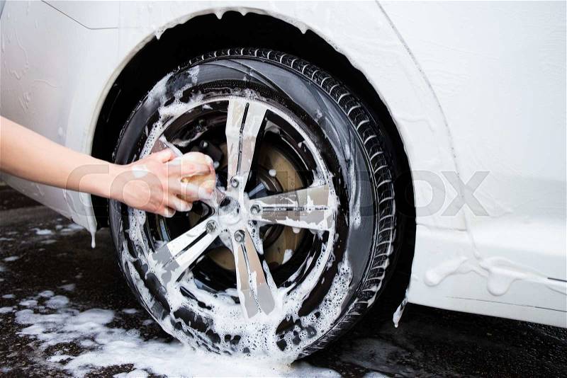 Male hand with foam sponge washing car wheel, stock photo