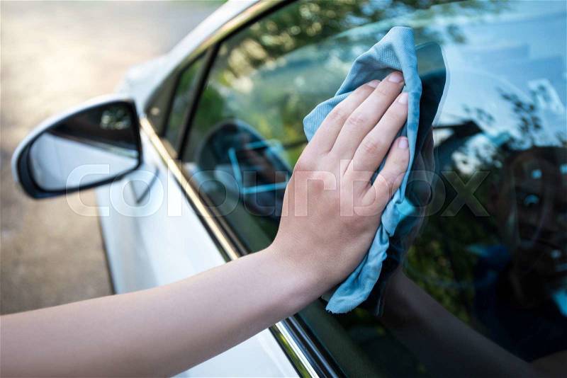 Male hand cleaning car window with blue microfiber cloth, stock photo