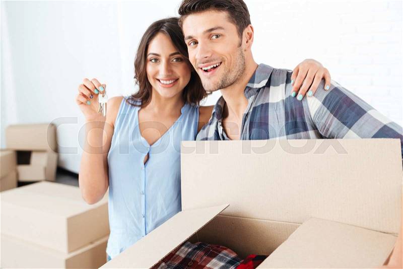 Couple showing keys to new home hugging looking at camera, stock photo