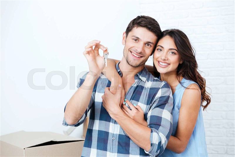 Young smiling couple showing keys to new home hugging looking at camera, stock photo