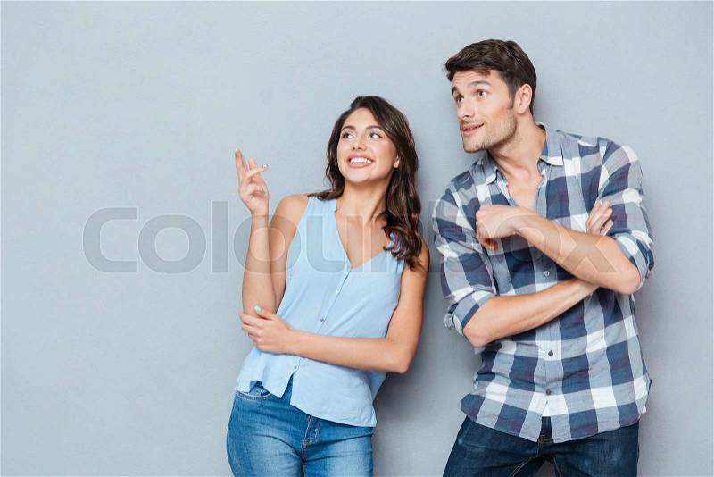Attractive smiling couple standing and pointing at something on white background, stock photo
