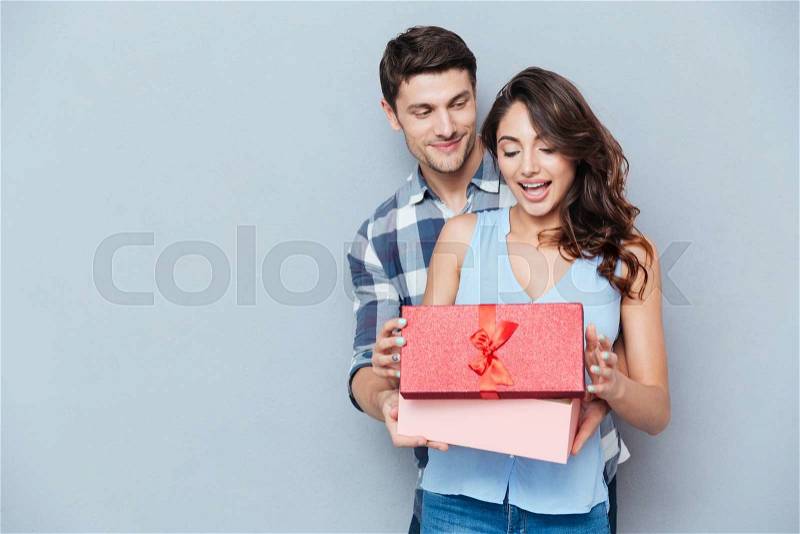Young beautiful woman receiving a gift from her boyfriend isolated on gray background, stock photo