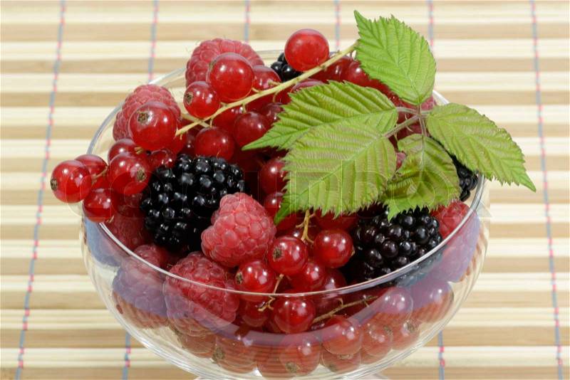 Different sorts of berries with leaves in a glass, stock photo